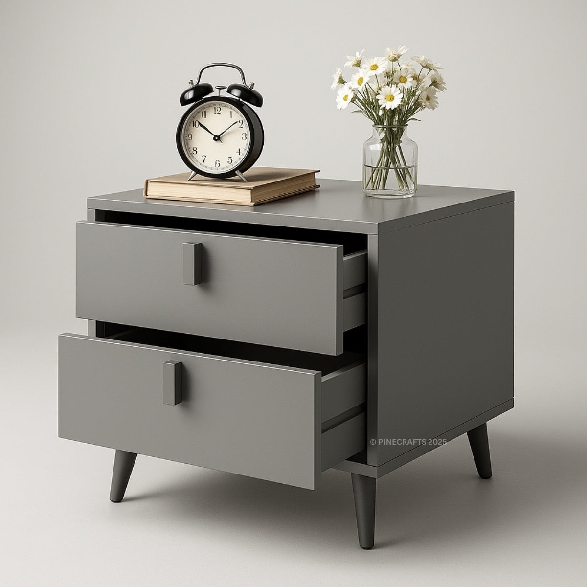 Gray dresser with two drawers, an alarm clock, book, and vase of flowers on a light gray background.